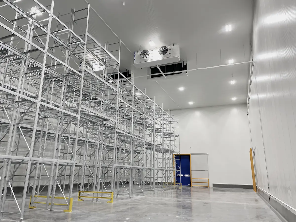 Interior de almacén vacío con estanterías metálicas y unidad de ventilación en el techo