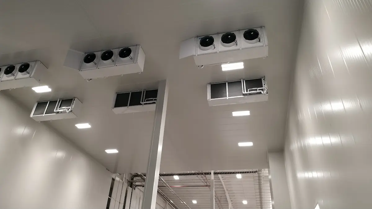 Ventiladores grandes y luces instalados en el techo de una sala industrial blanca.