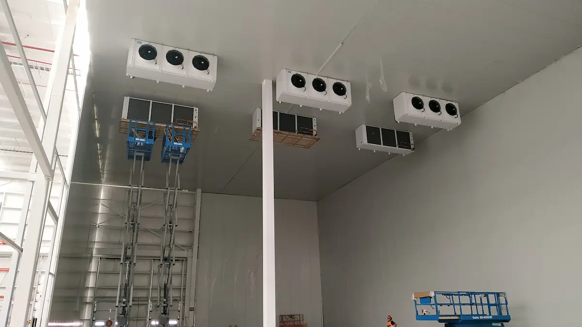 Un interior industrial con unidades de ventilación instaladas en el techo y plataformas elevadoras azules.