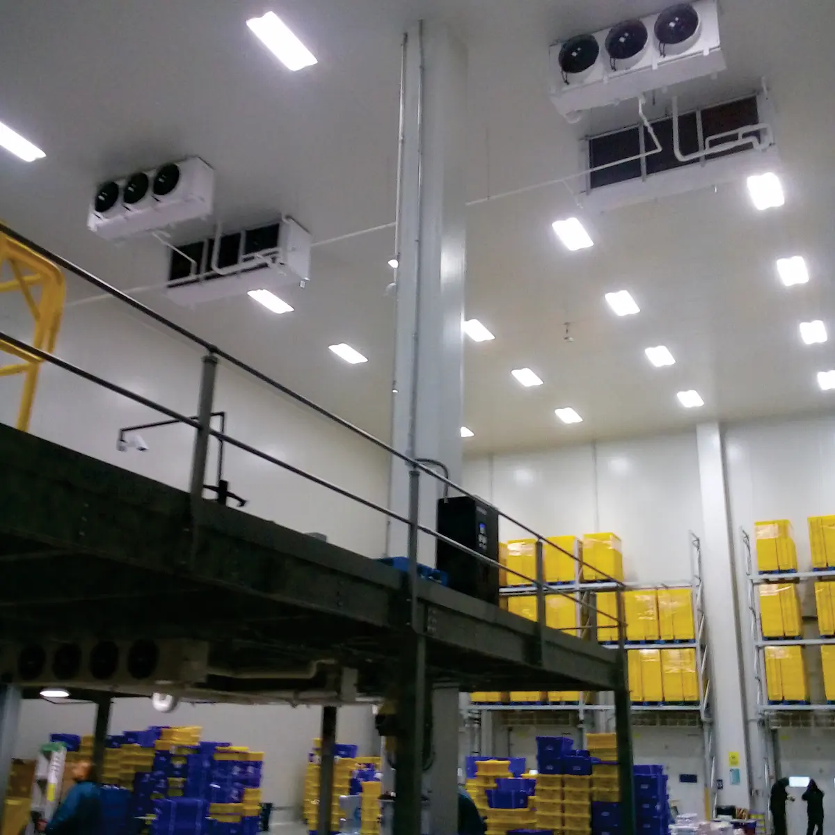 Almacén con estanterías altas llenas de cajas amarillas y azules y sistemas de refrigeración en el techo.