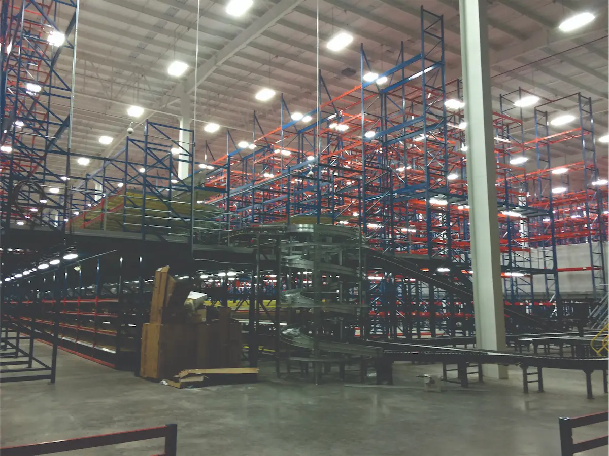 Interior de un almacén con estanterías altas de metal azul y naranja y transportadores en espiral.