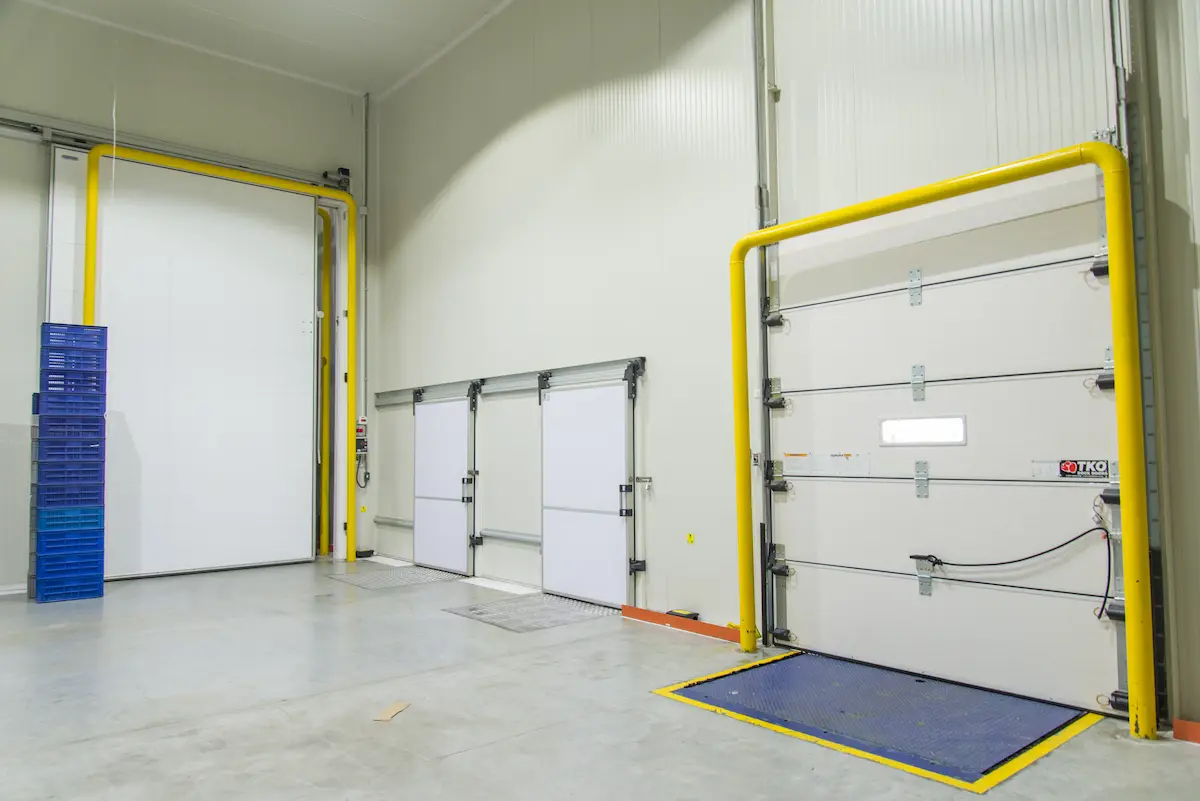 Interior de almacén con puertas industriales blancas y tubería amarilla en paredes.