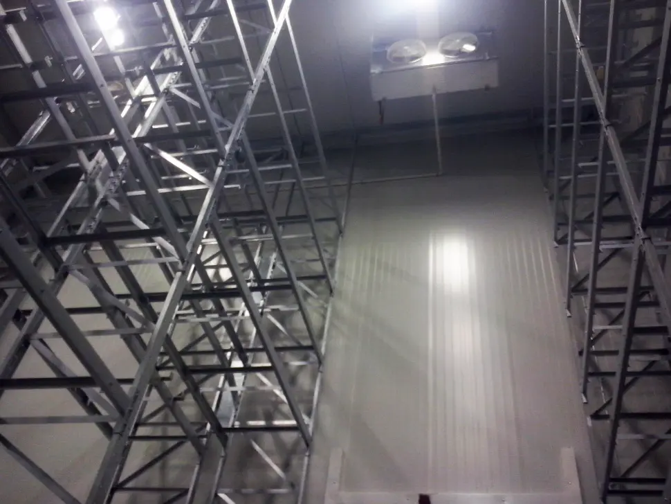 Estructura metálica y pared blanca alta con iluminación en el techo interior de un almacén.