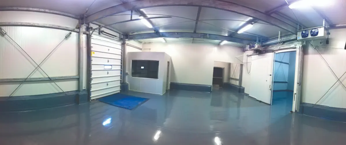 Interior de almacén industrial con pisos grises brillantes y dos puertas grandes corredizas.