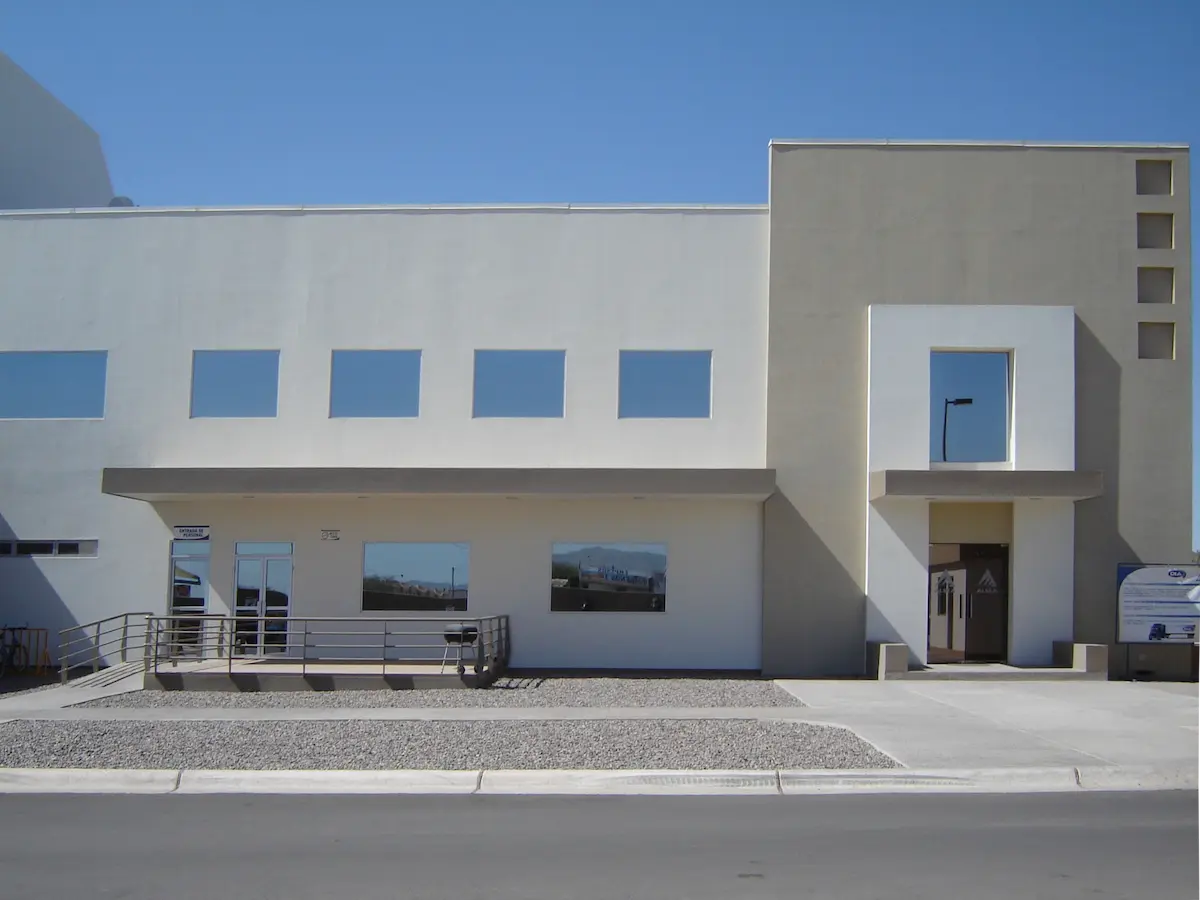 Edificio blanco moderno con ventanas cuadradas y entrada principal en un día soleado.