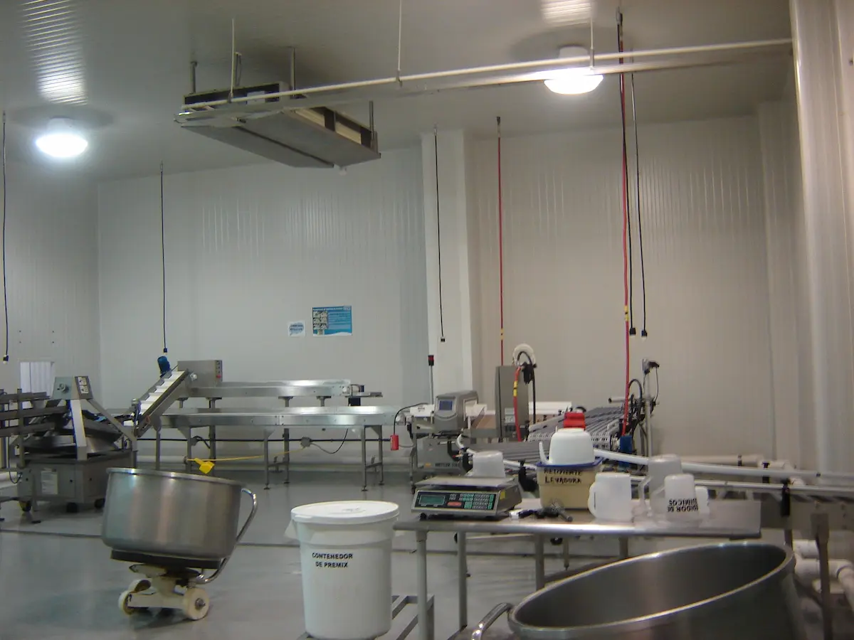 Interior de una planta de procesamiento con mesas, contenedores y equipo industrial.