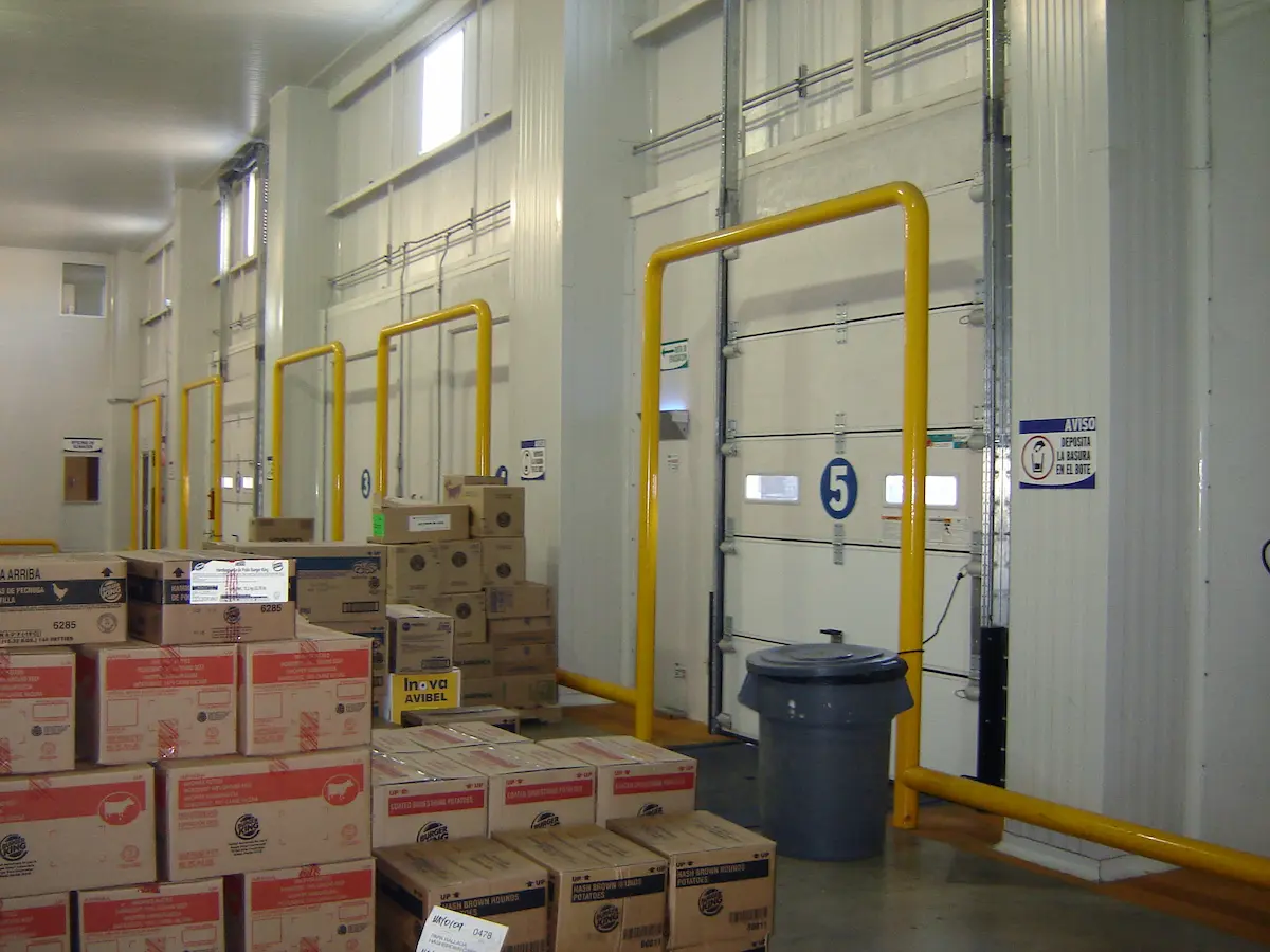 Interior de almacén con cajas apiladas y puertas de carga numeradas del 3 al 5.