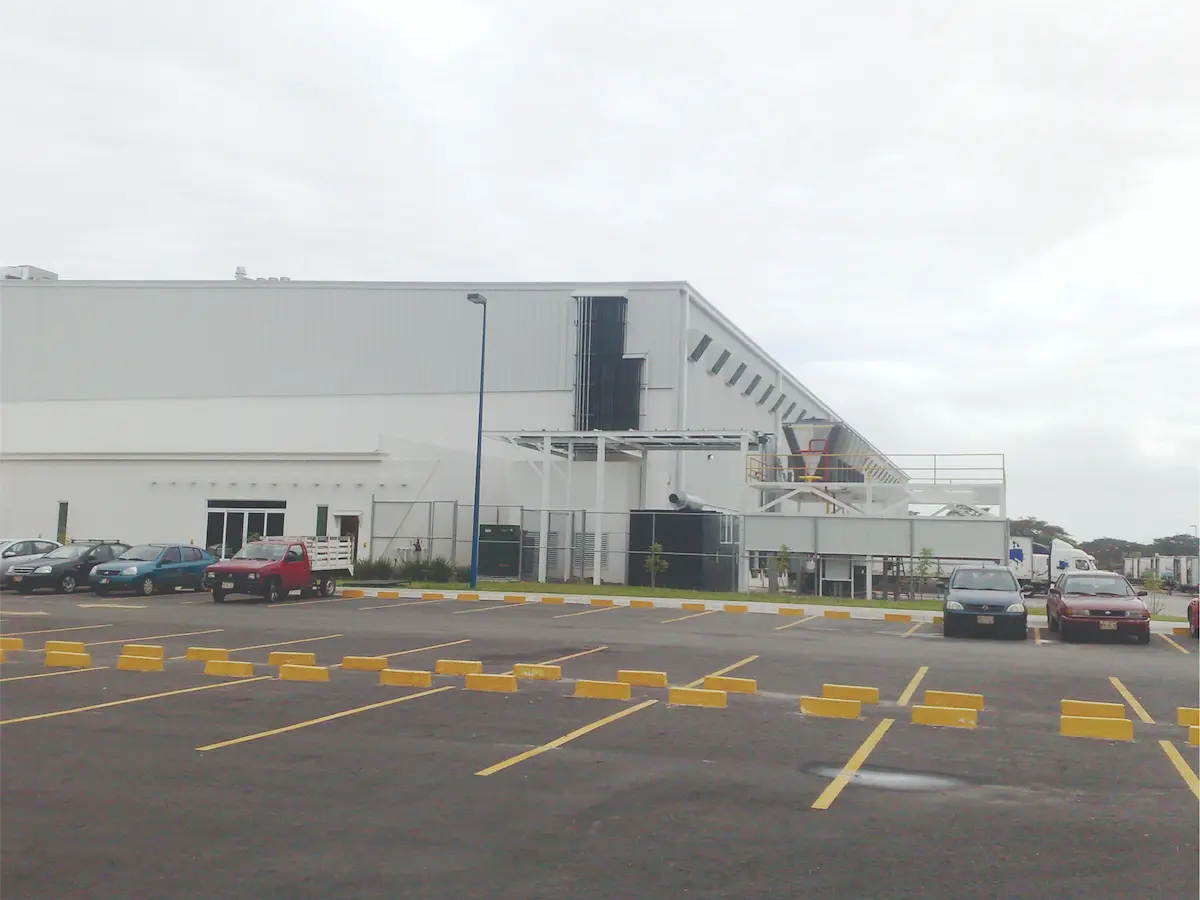 Estacionamiento con coches frente a un edificio industrial blanco bajo cielo nublado.