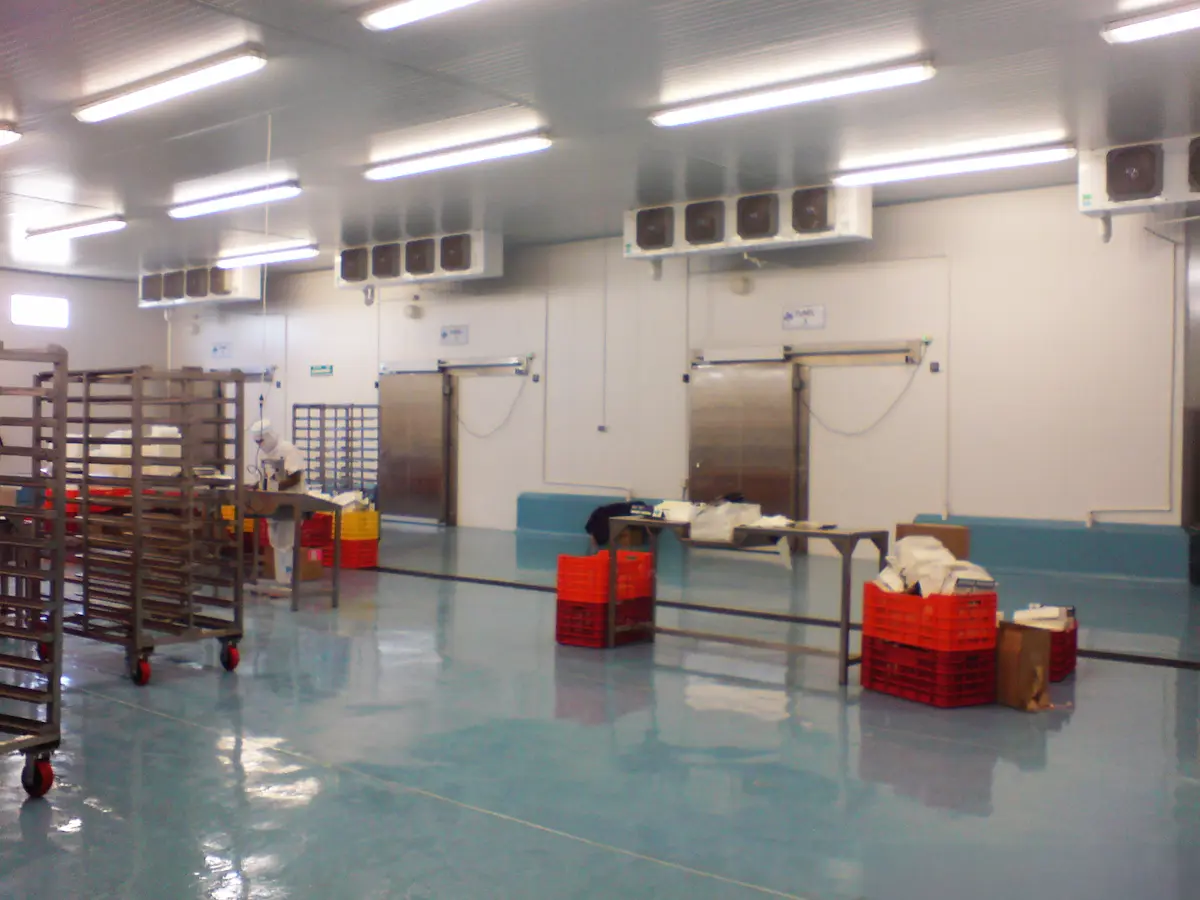 Interior de sala de producción con pisos brillantes, carritos, mesas y un trabajador con equipo de protección.