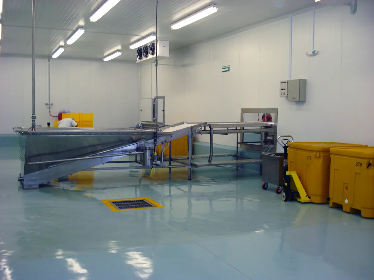 Interior de planta industrial con maquinaria metálica y contenedores amarillos en piso pulido.