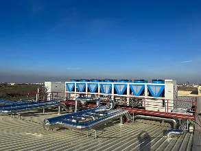 Equipos industriales azules en una azotea con cielo azul claro y horizonte urbano.