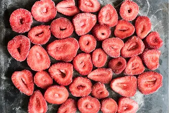 Fresas congeladas en rodajas extendidas sobre una superficie negra.