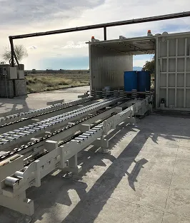 Línea de producción con cintas transportadoras frente a un contenedor industrial abierto en un área al aire libre.