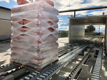 Palé envuelto en plástico en una máquina transportadora al aire libre bajo un cielo azul.