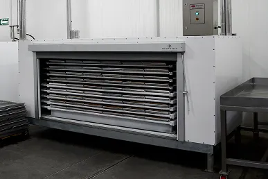 Congelador de placas industrial con bandejas metálicas apiladas en su interior en una sala blanca.