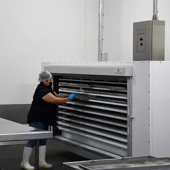 Trabajadora con gorro y guantes usando un congelador de placas industrial en sala limpia.