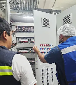 Dos técnicos operan un panel eléctrico industrial con múltiples botones y medidores.