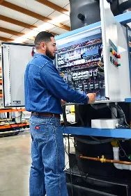 Hombre revisa componentes de un panel eléctrico abierto en un taller industrial.