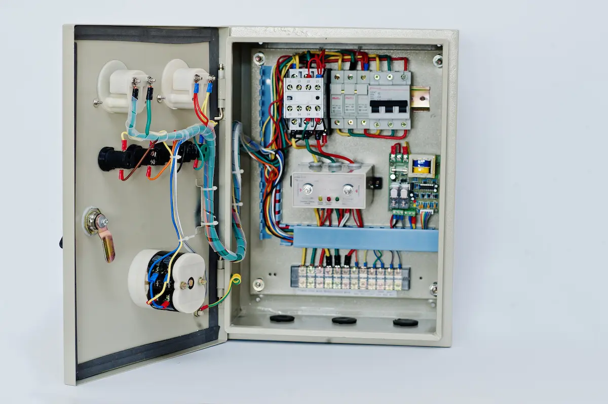 Panel de control eléctrico abierto con varios cables y componentes conectados en caja metálica.