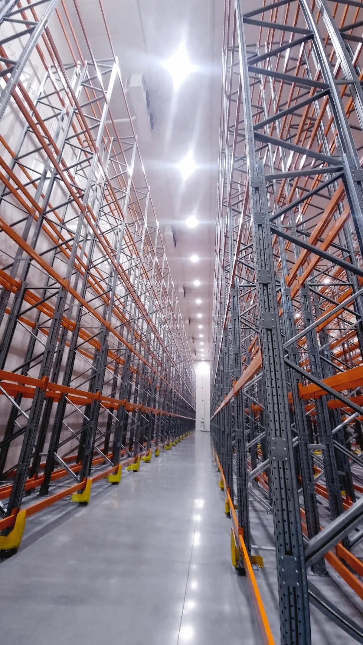 Pasillo limpio entre estantes metálicos altos de almacenaje en un gran almacén vacío y bien iluminado.