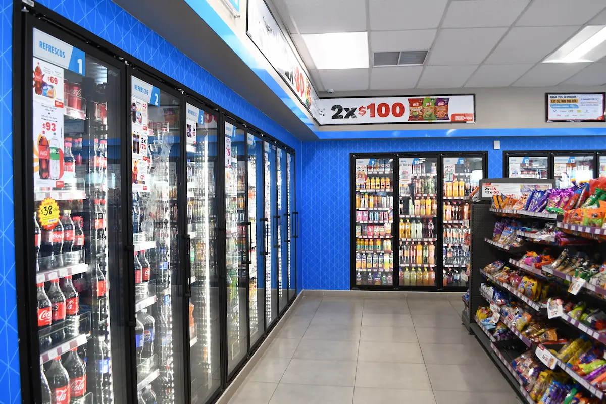 Pasillo de tienda con refrigeradores de bebidas y estantes con botanas en exhibición.
