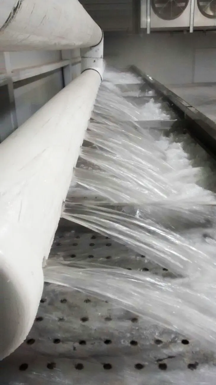 Tubería blanca que descarga chorros de agua claros sobre una superficie metálica perforada.