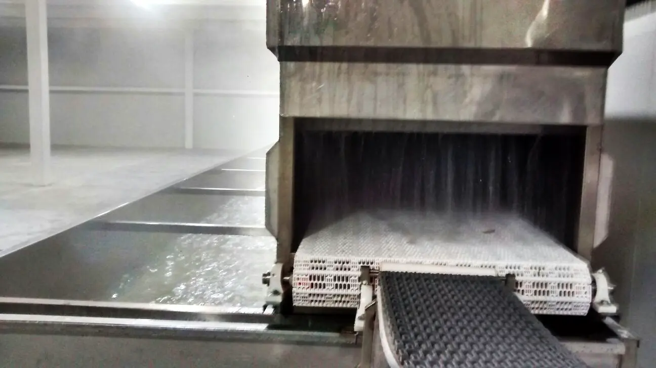 Máquina industrial con cinta transportadora y flujo de agua para enfriar o limpiar productos.