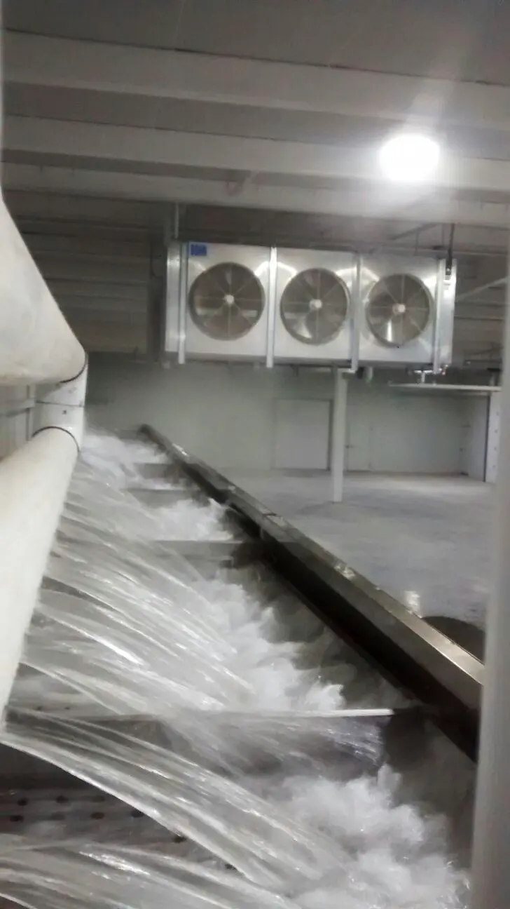 Máquina industrial con flujo fuerte de agua y ventiladores grandes en un espacio cerrado.