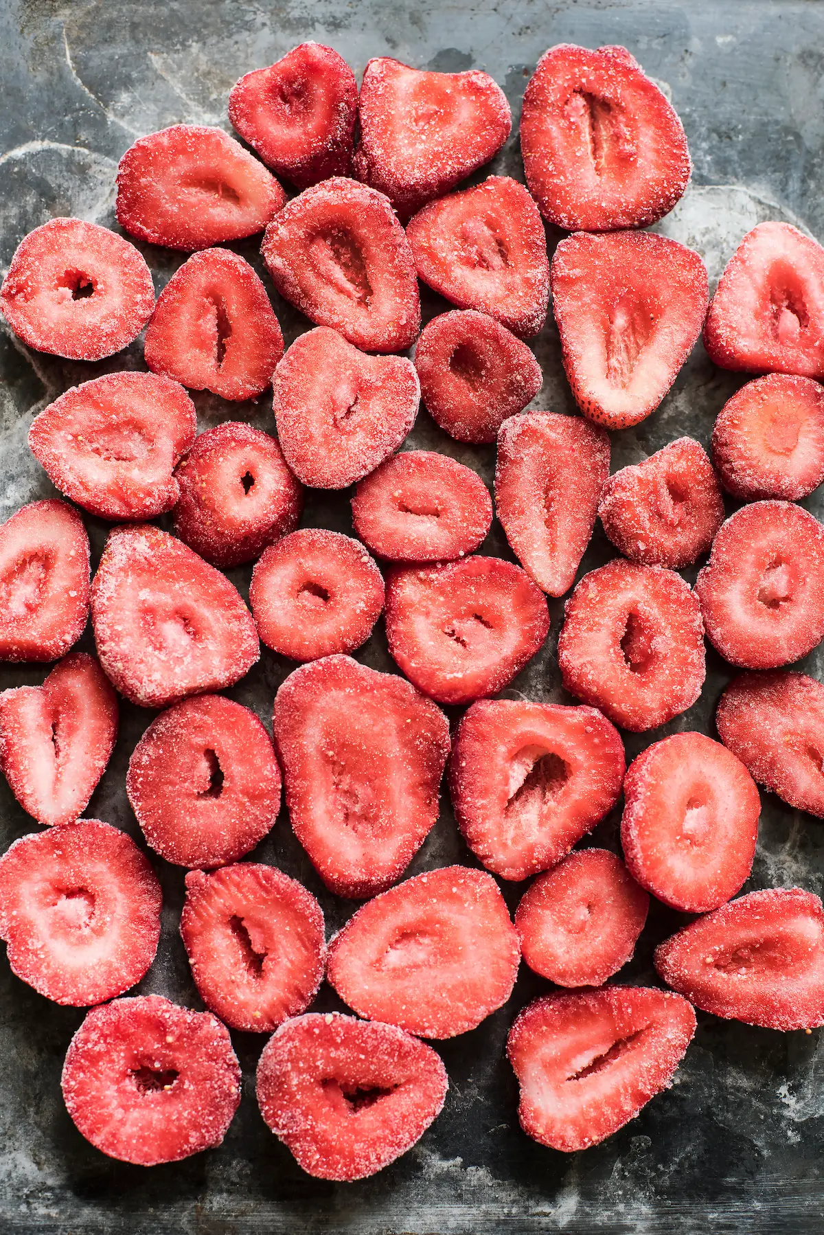 Fresas congeladas cortadas por la mitad dispuestas sobre una superficie oscura.