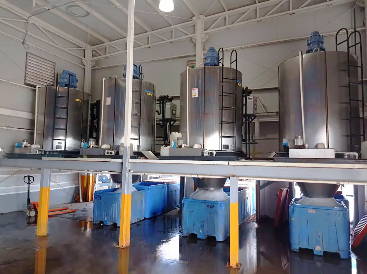 Instalación industrial con tanques metálicos grandes y contenedores azules para hielo.