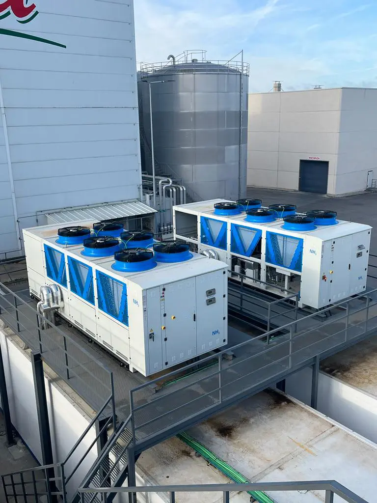 Dos unidades industriales blancas con ventiladores azules sobre estructura metálica en edificio industrial.