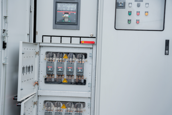 Gabinete eléctrico abierto con interruptores y panel de control con botones en una sala técnica.