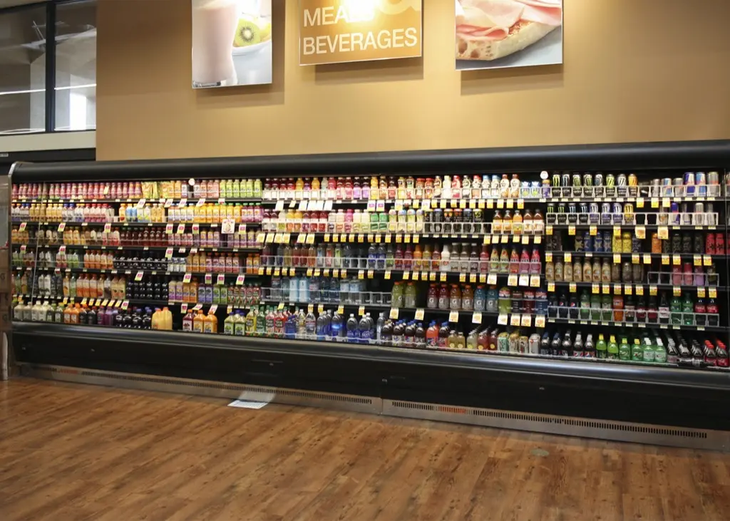 Estantería de supermercado con diversas bebidas frías en botellas y latas.