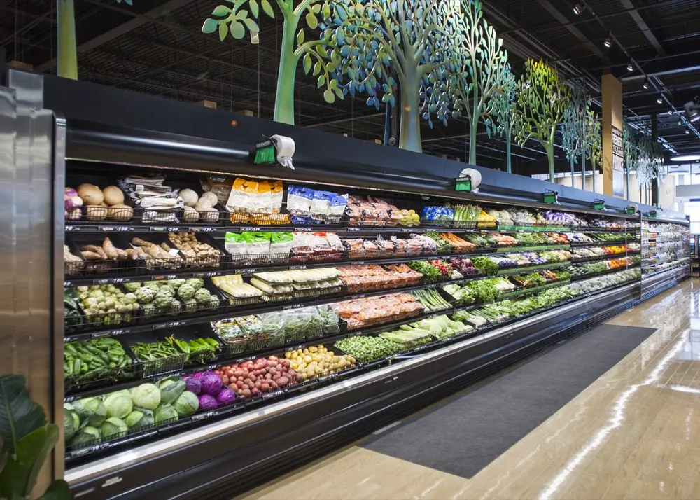 Pasillo largo con estantes llenos de verduras frescas variadas en un supermercado moderno.