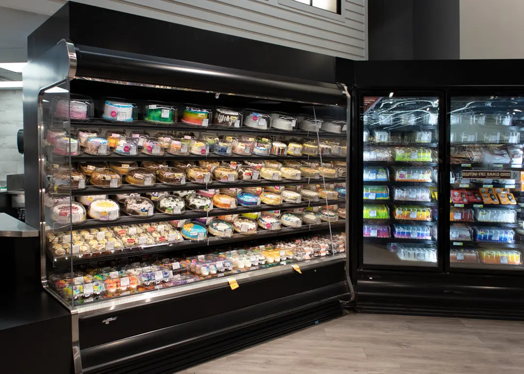 Vitrinas de refrigerador con pasteles, postres en envases plásticos y productos horneados.