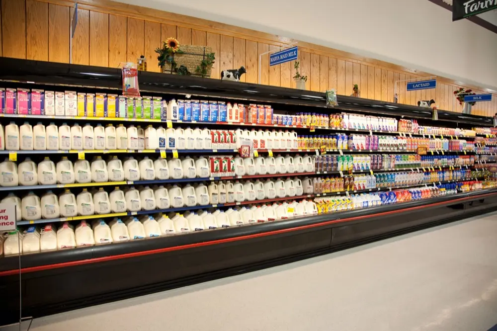 Estantería larga en supermercado con leche y productos lácteos ordenados por tipos y marcas.