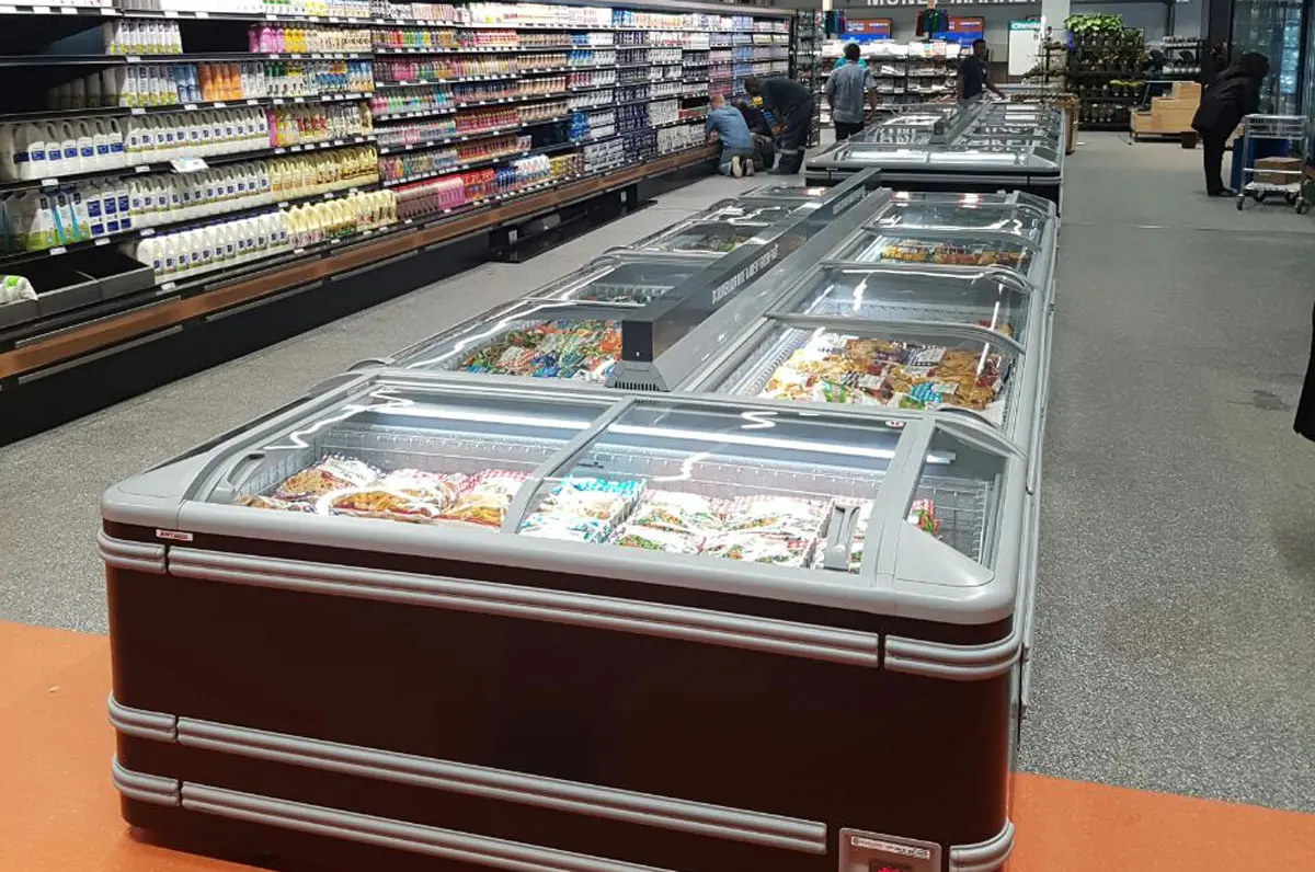 Congeladores en supermercado con productos congelados visibles y clientes al fondo.