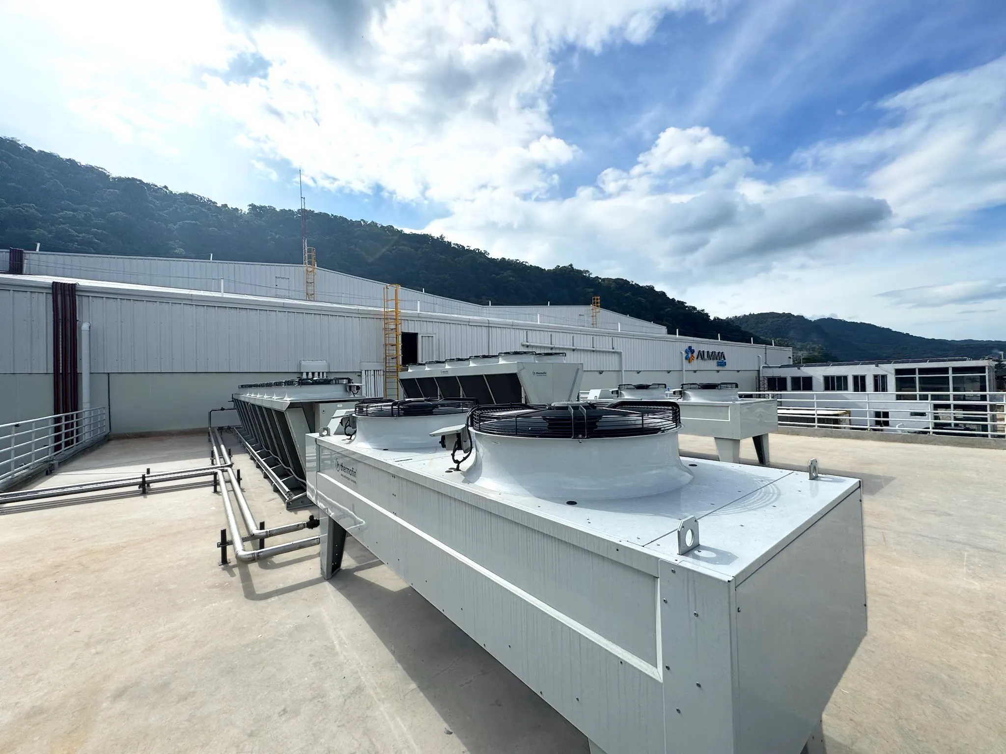 Unidades grandes de aire acondicionado tipo industrial en un techo con montañas y cielo nublado.