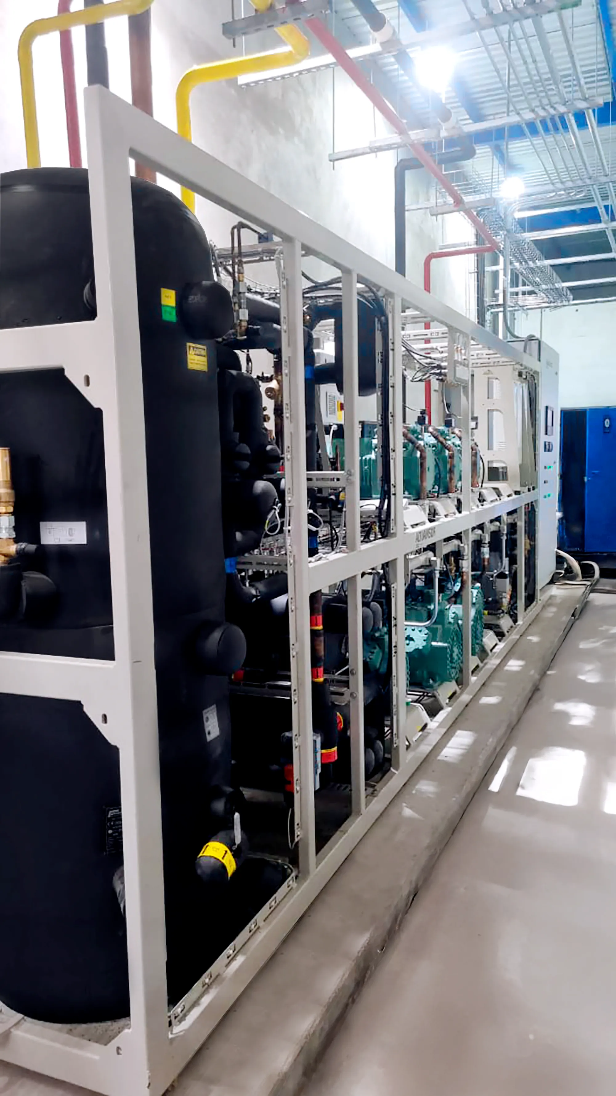 Sistema industrial de refrigeración con tuberías y compresores en un espacio técnico limpio.