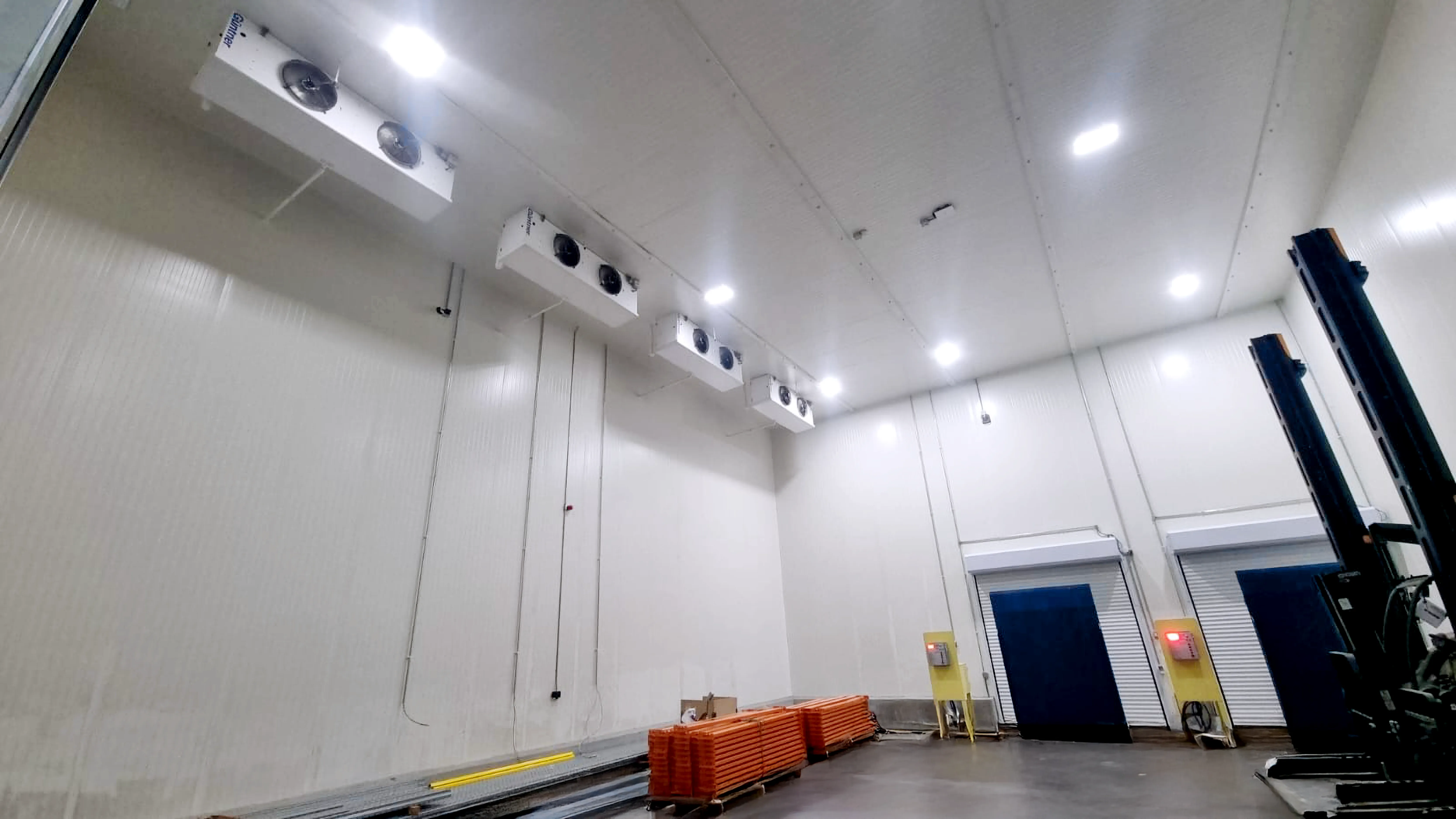 Interior de una cámara frigorífica con ventiladores de techo y equipo de elevación a la derecha.