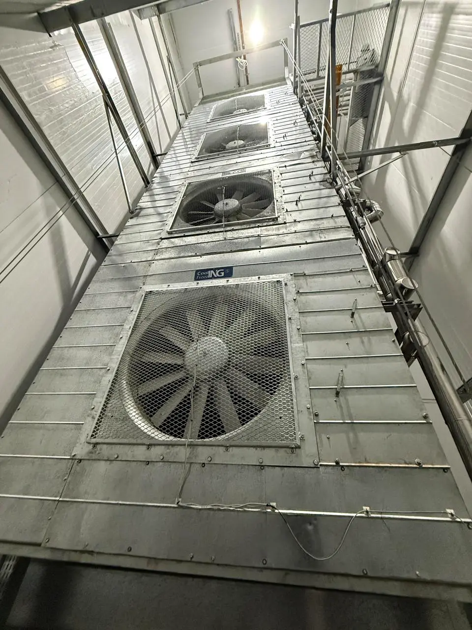 Torre alta con cuatro grandes ventiladores industriales en interior metálico de planta fría.