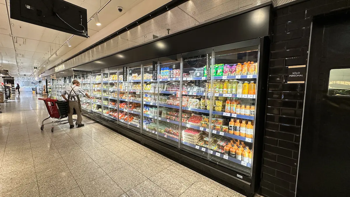 Persona con carrito de compras mientras selecciona productos en los refrigeradores de un supermercado.
