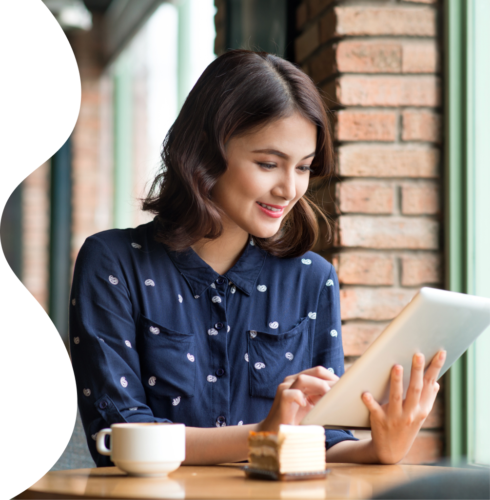 Woman smiling and using a tablet at a cafe table with a cup of coffee and a slice of cake.