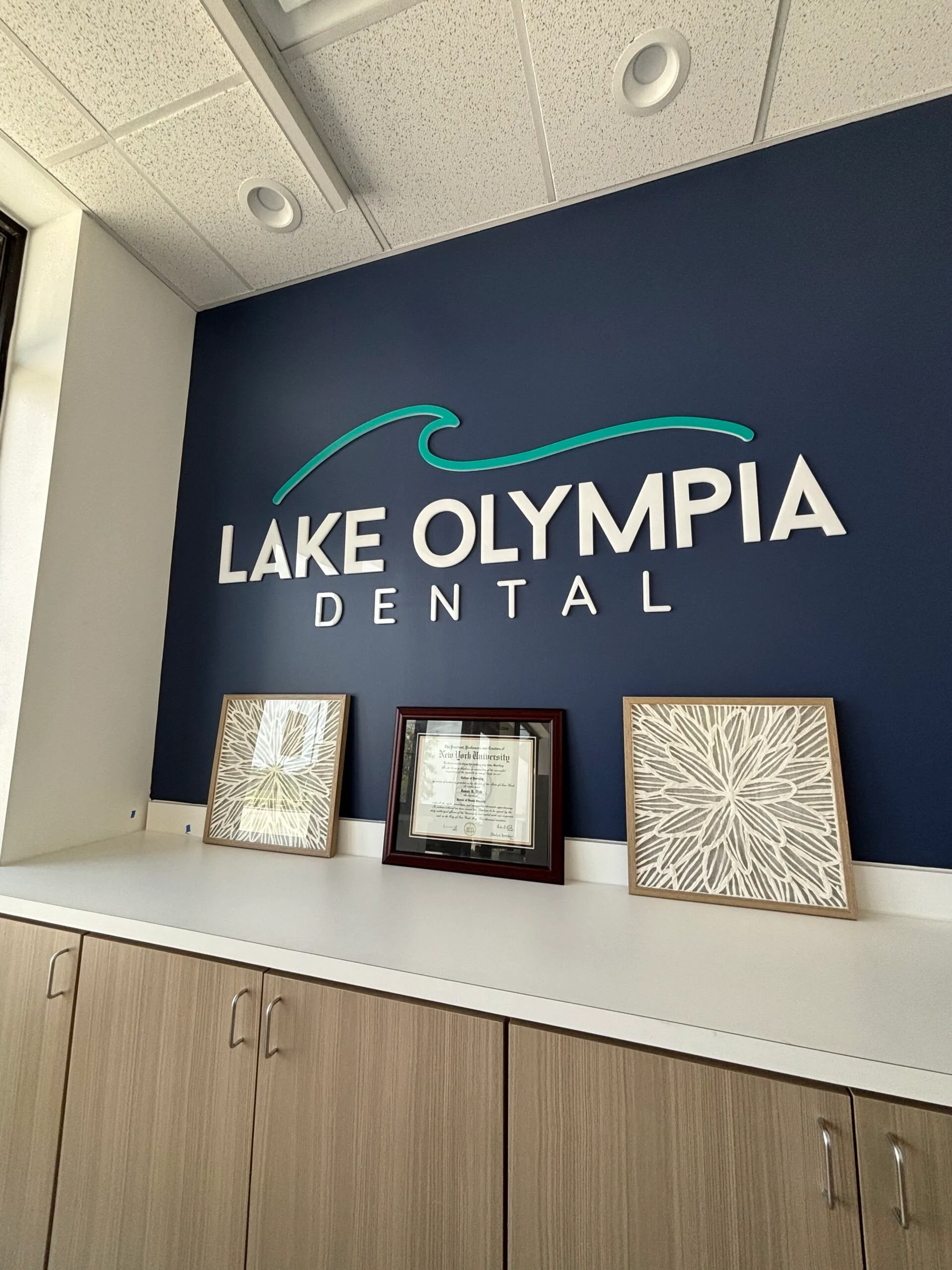 Reception area of Lake Olympia Dental with a blue wall, white signage, and three framed decorations on a countertop.