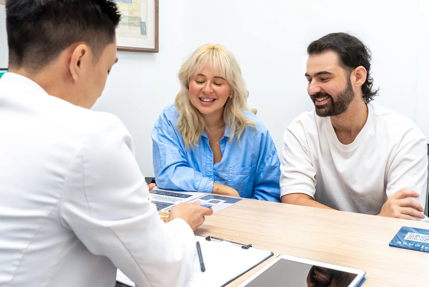A doctor in a white coat discussing information with a smiling couple sitting at a desk.