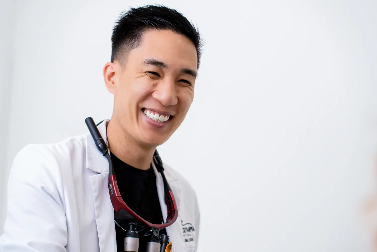 Smiling male dentist wearing a white coat and dental loupe around his neck.