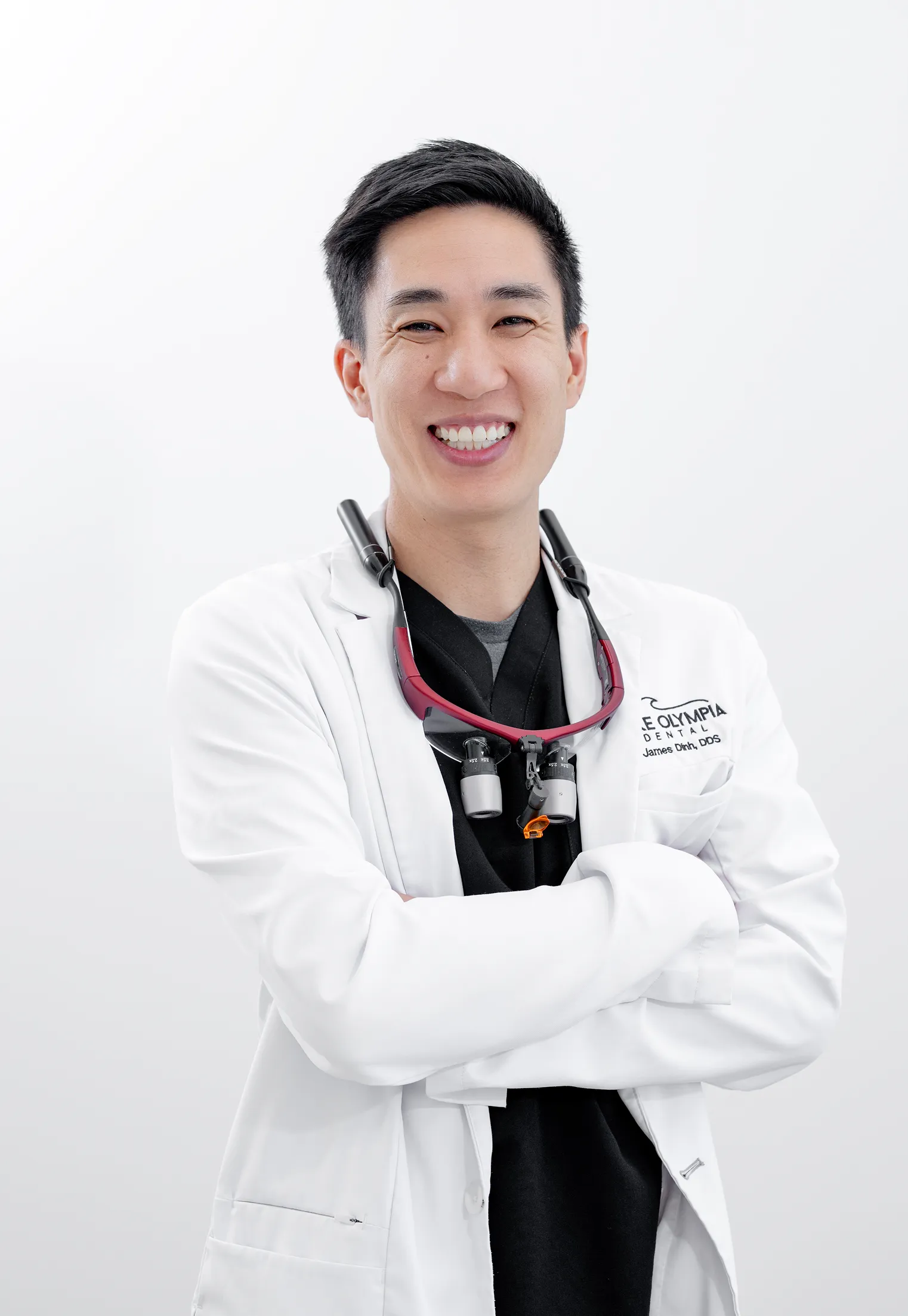 Smiling male dentist in white coat with dental magnifying glasses around his neck.