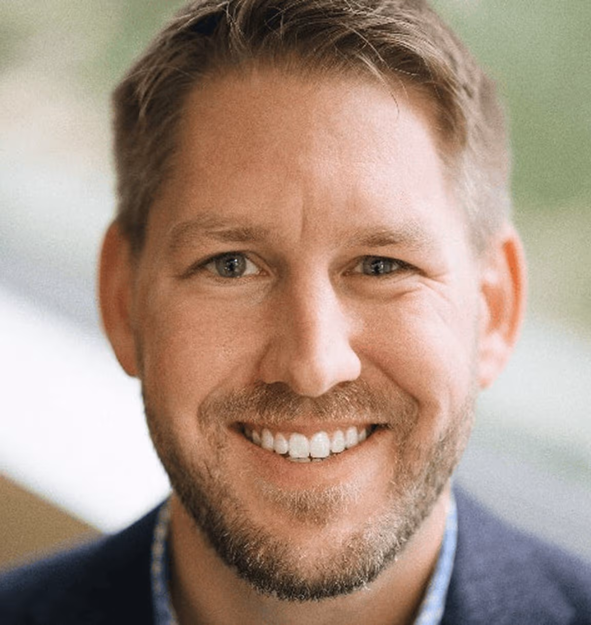 Close-up of a smiling man with short light brown hair, light beard, and blue eyes.