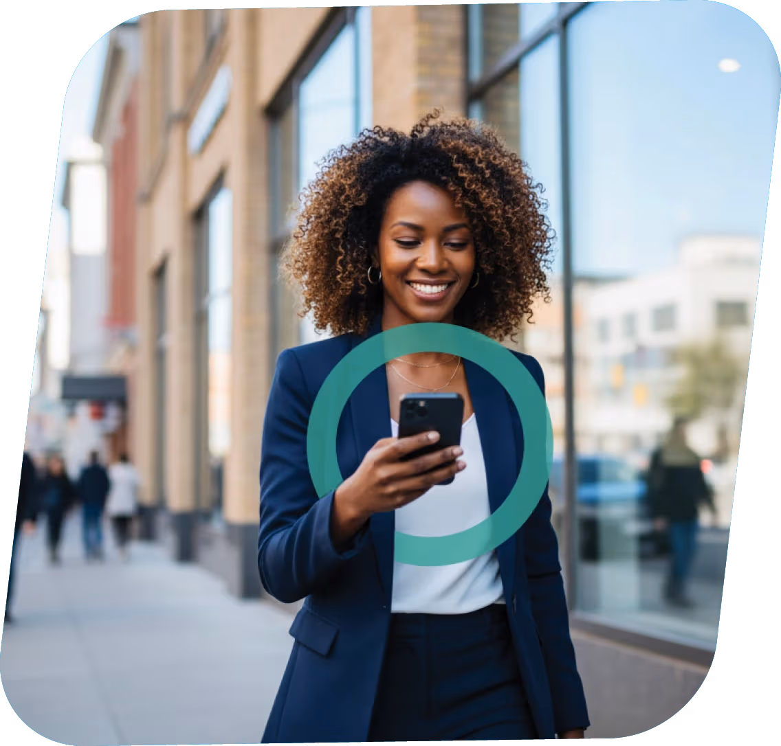 Smiling woman in business attire looking at her smartphone while walking on an urban sidewalk.