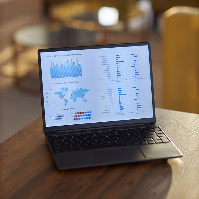 Open laptop on wooden table displaying website analytics with graphs, a world map of customer activity, and traffic statistics.